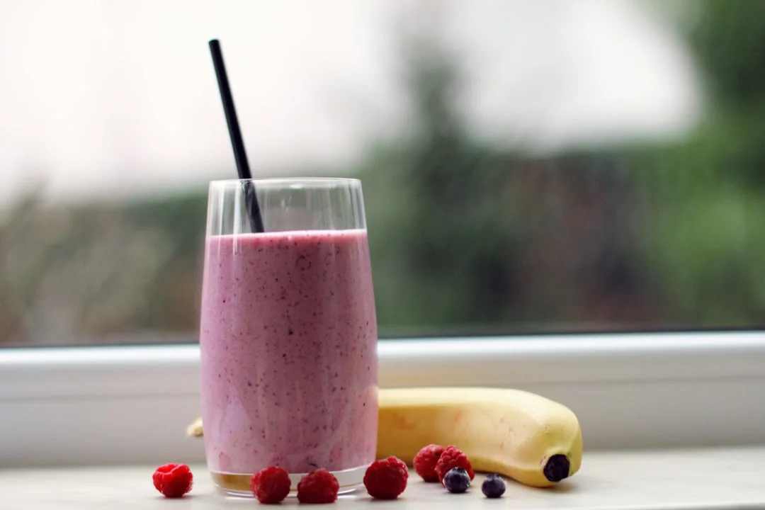 A Vitamix blender on a clean kitchen counter surrounded by fresh spinach, frozen mango chunks, spirulina powder, and a small bowl of collagen peptides, morning light streaming in from the side